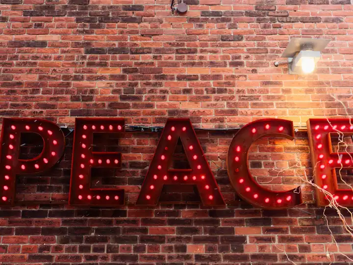 Red bulb-lit letters spelling PEACE on a brick wall